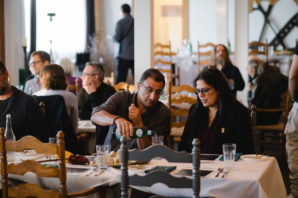 Guests sitting at tables during a dinner event, with someone pouring water into a glass.